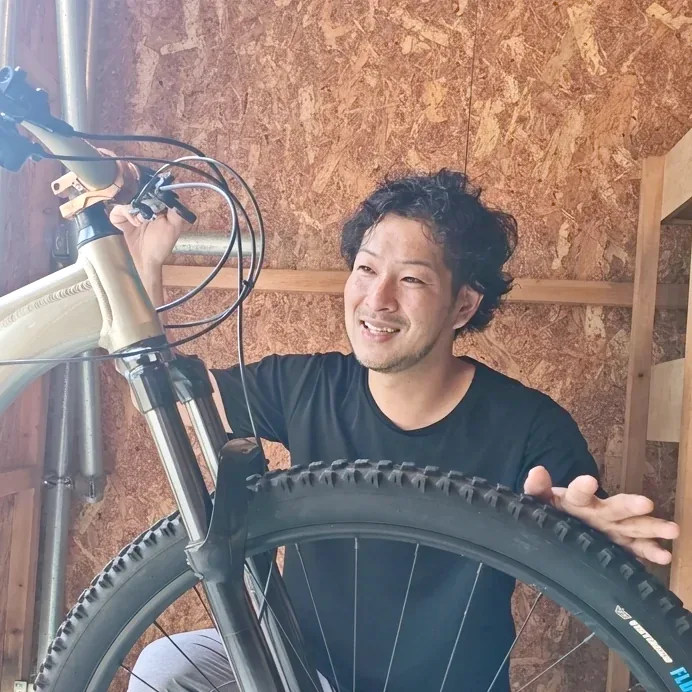 めぐり自転車の高多優典（たかた まさのり）。整備中のマウンテンバイクの前で